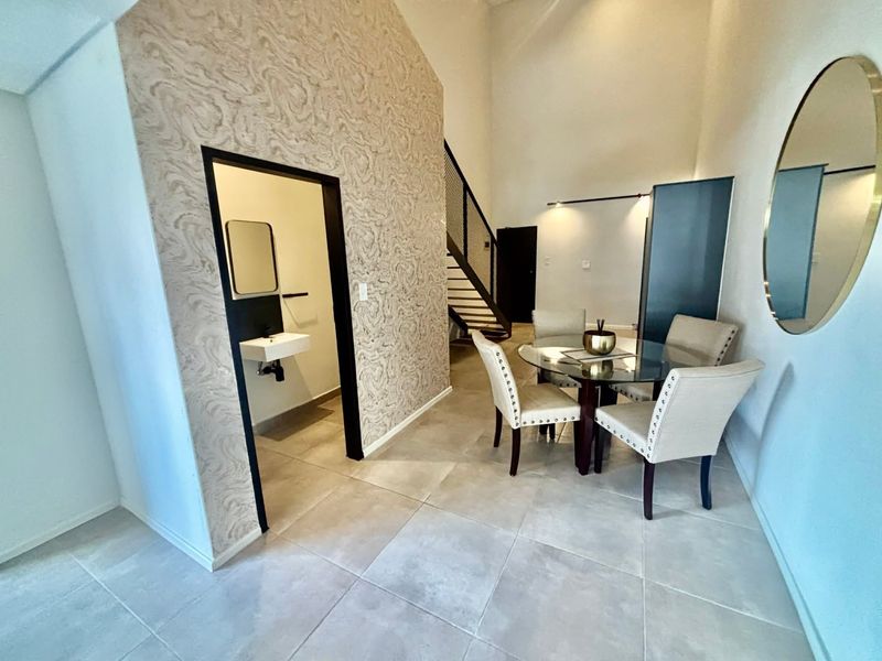 Open plan living area featuring tiled flooring, a feature wall with textured wallpaper, and a modern staircase leading to the upper level.