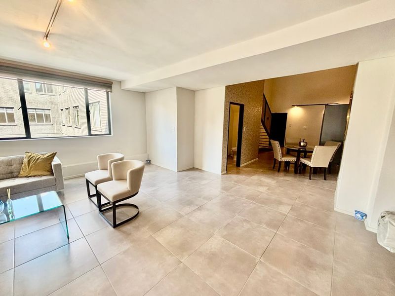 Spacious open-plan living area featuring large format floor tiles, modern track lighting, and large windows allowing for ample natural light.