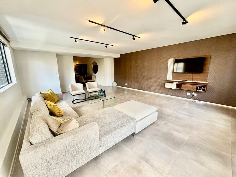 Spacious living room featuring modern track lighting, large format floor tiles, and a built-in media console against a textured feature wall.