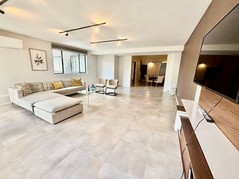 Spacious open-plan living area featuring large format floor tiles, modern track lighting, and a built-in media console, seamlessly connecting to the dining space.
