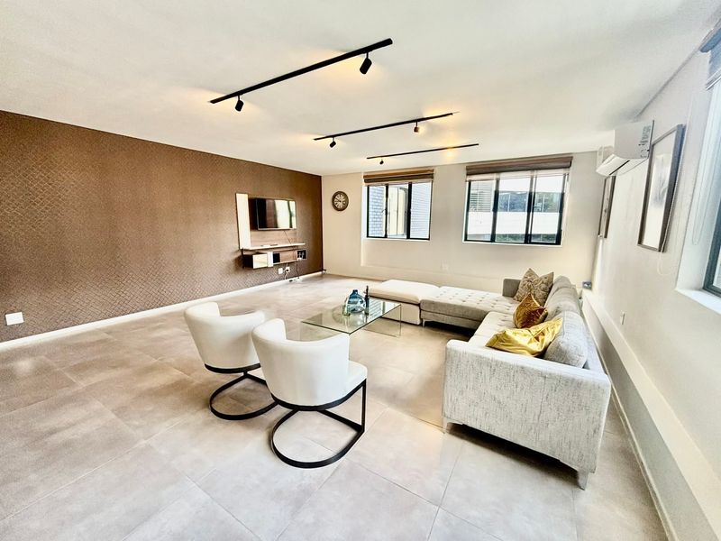 Spacious living room featuring large format floor tiles, a textured feature wall, modern track lighting, and a wall-mounted media console.