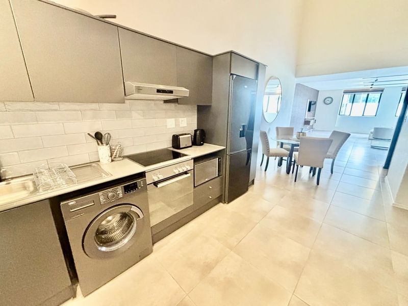 Modern open-plan kitchen featuring sleek grey cabinetry, subway tile backsplash, and integrated appliances, flowing seamlessly into the dining and living area.