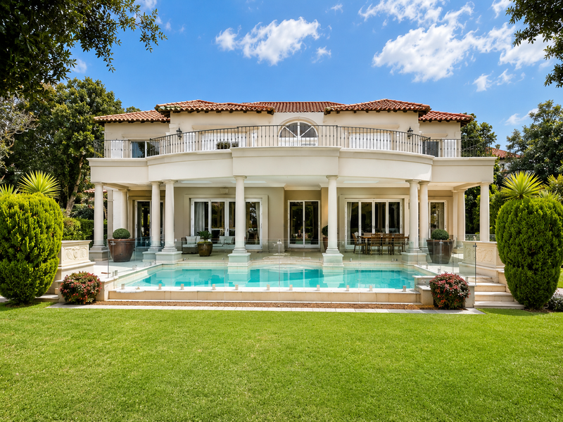 Rear elevation of a luxury cluster home featuring a swimming pool, glass fencing, covered patio, and an upper-level balcony with wrought iron railings.