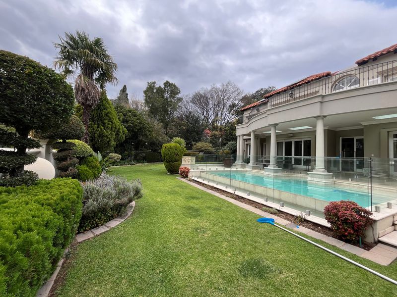 A well-maintained rear garden featuring a swimming pool with glass fencing, a covered patio area, and an upper-level balcony.
