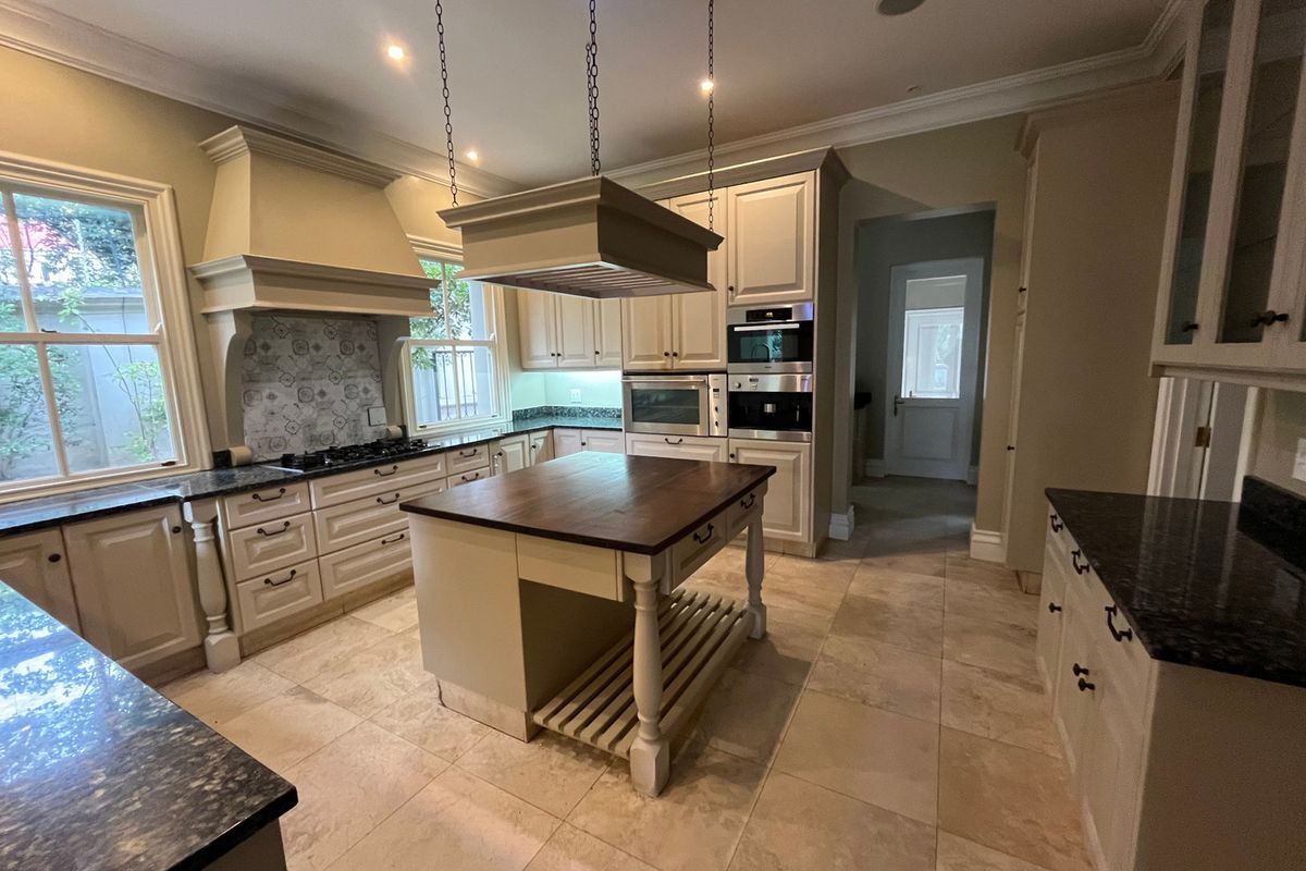 Spacious kitchen featuring classic cabinetry, granite countertops, a central island with a wooden top, and integrated appliances including a gas hob and built-in ovens.