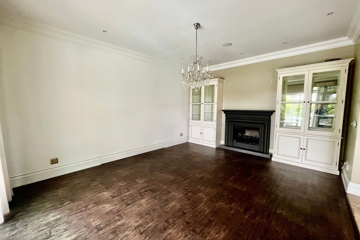 Spacious living room featuring dark hardwood flooring, built-in display cabinetry, a classic fireplace, and elegant crown molding.