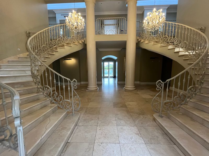 Grand entrance hall featuring a dual sweeping staircase with wrought iron balustrades, stone flooring, and elegant crystal chandeliers.