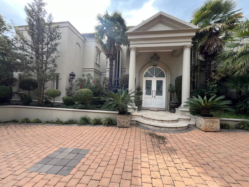 Elegant front entrance featuring a grand portico with columns, stone steps, and a paved driveway leading to a double-door entryway.