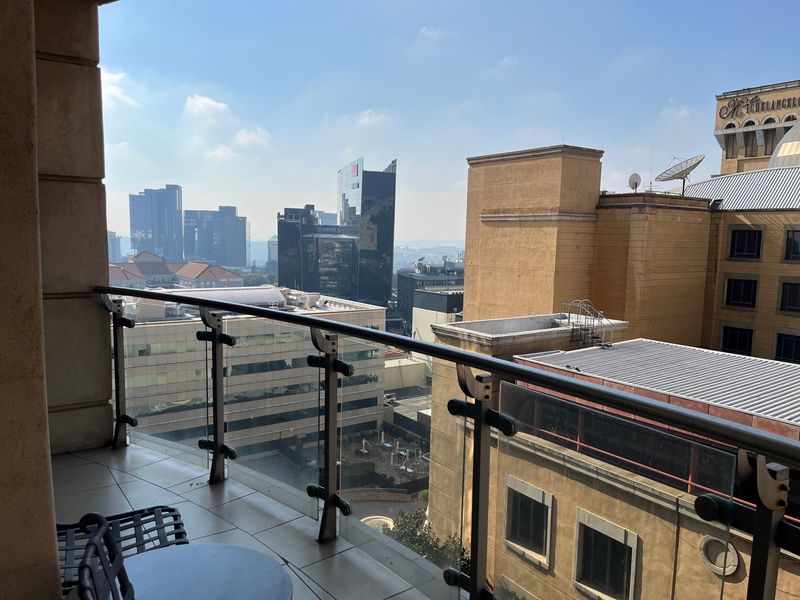 A private balcony featuring a modern glass balustrade and tiled flooring, offering an elevated urban view of the surrounding city skyline.