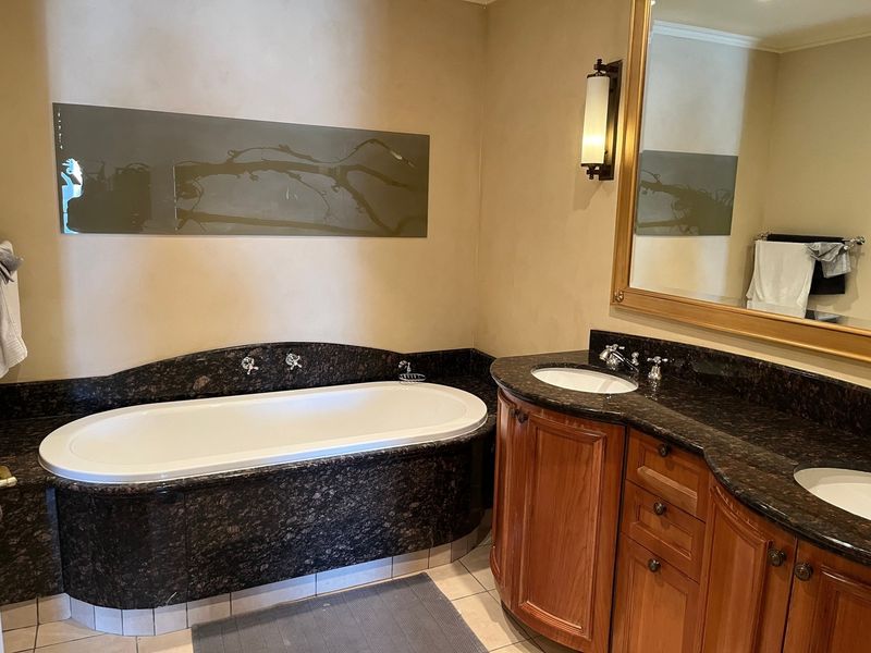 A spacious bathroom featuring a built-in bathtub with granite surround, a double vanity with wooden cabinetry, and granite countertops.