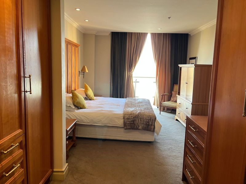 A spacious bedroom featuring built-in wooden cabinetry, carpeted flooring, recessed lighting, and direct access to a balcony through large sliding doors.