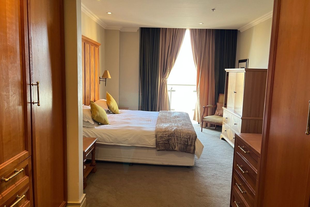 A spacious bedroom featuring built-in wooden cabinetry, carpeted flooring, recessed lighting, and direct access to a balcony through large sliding doors.
