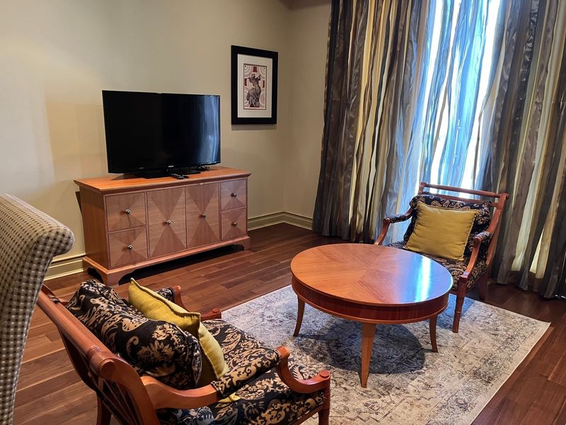 A well-maintained living room featuring rich hardwood flooring and floor-to-ceiling window treatments, creating a warm and inviting atmosphere.