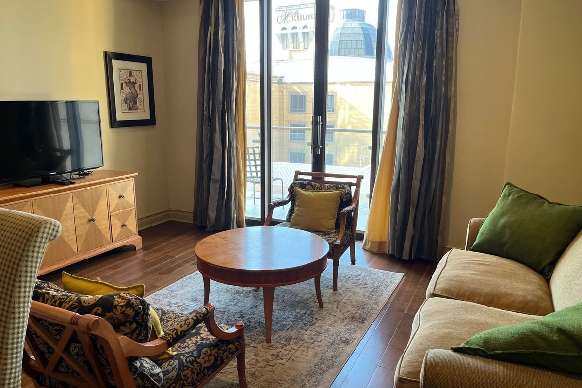 A comfortable living room featuring hardwood flooring, crown molding, and large sliding glass doors that provide access to a balcony with city views.