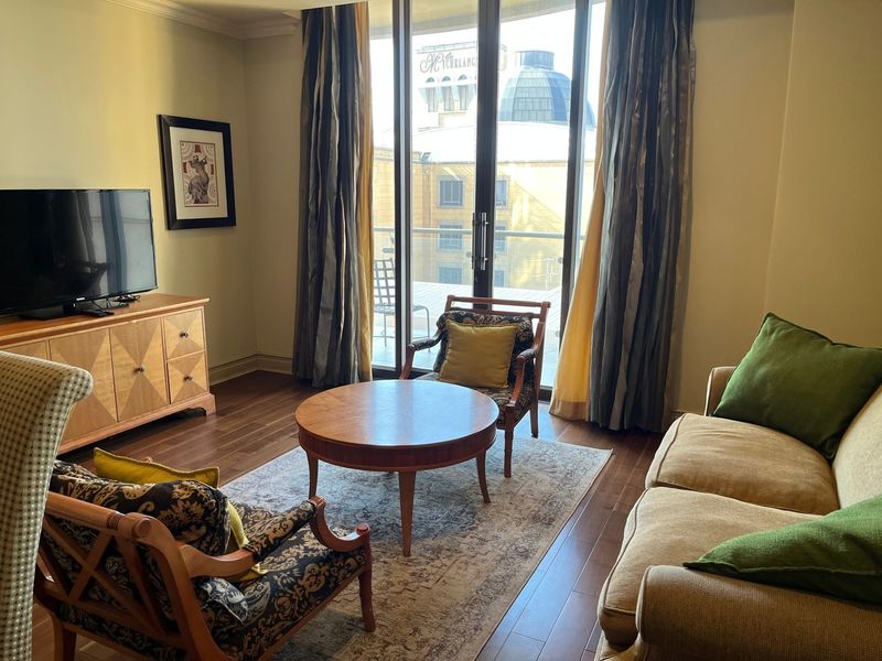 A comfortable living room featuring hardwood flooring, crown molding, and large sliding glass doors that provide access to a balcony with city views.