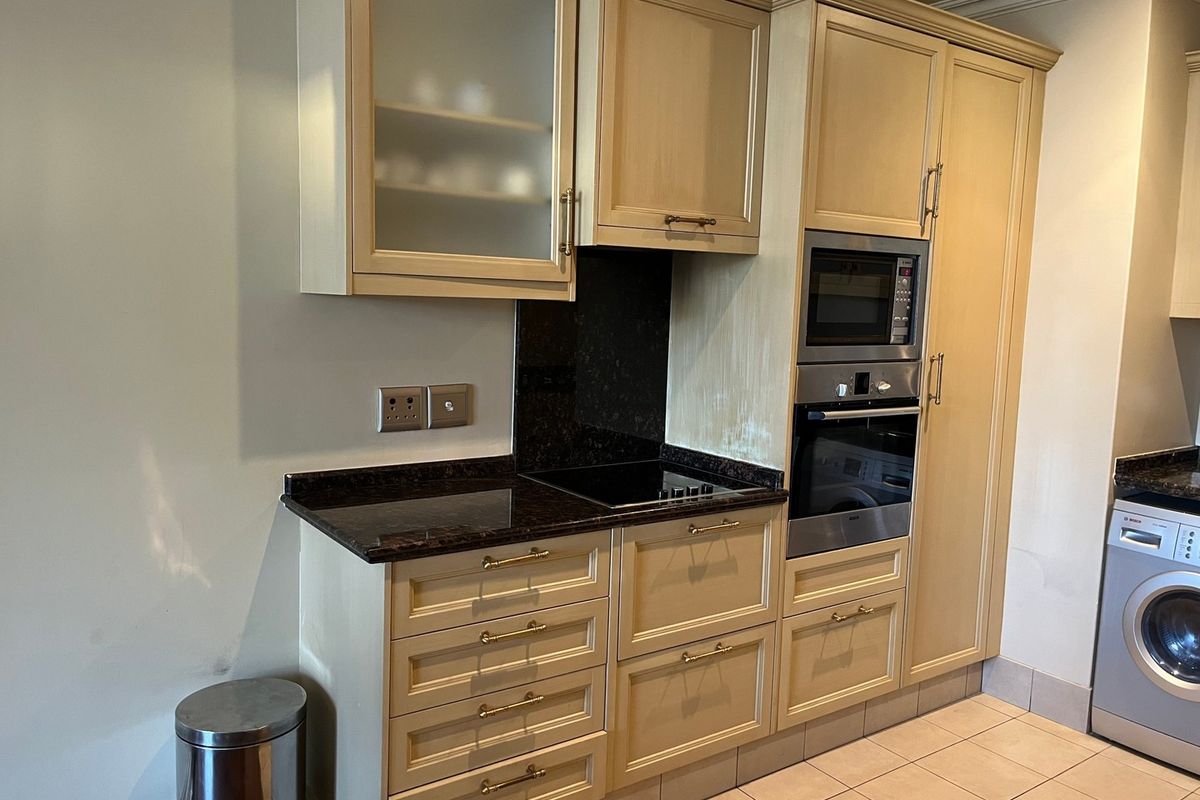 A functional kitchen featuring light-toned cabinetry, granite countertops, integrated appliances including an oven, microwave, and washing machine, with neutral tiled flooring.