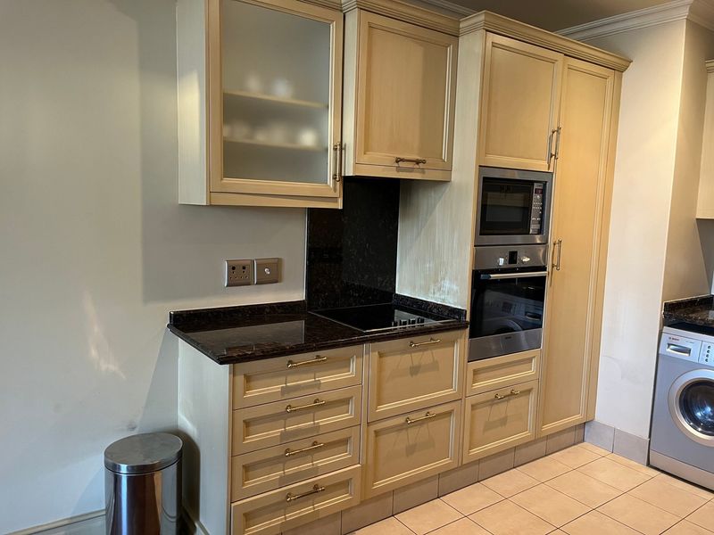 A functional kitchen featuring light-toned cabinetry, granite countertops, integrated appliances including an oven, microwave, and washing machine, with neutral tiled flooring.