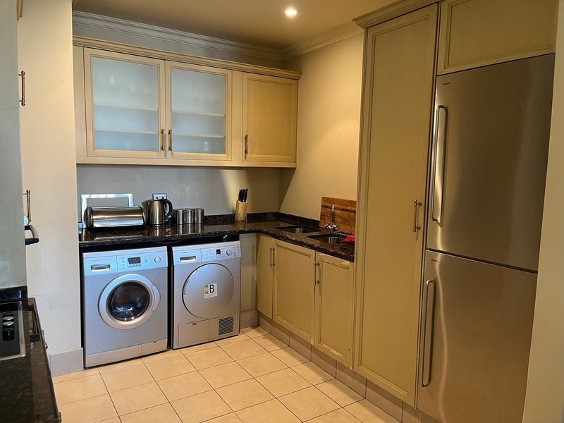 A functional scullery featuring built-in cabinetry, granite countertops, an integrated fridge-freezer, and dedicated space for laundry appliances.