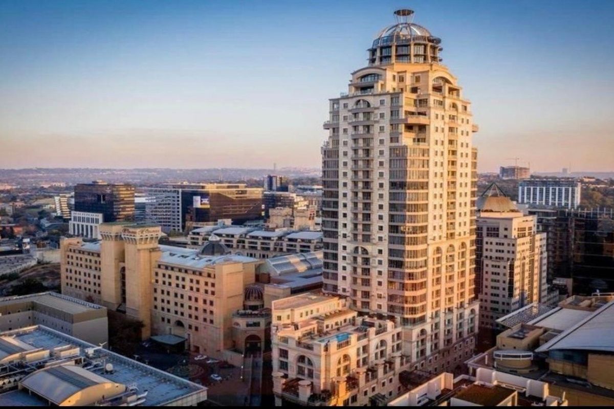 An aerial view of a prominent high-rise apartment building within a dense urban cityscape, showcasing its architectural design and surrounding infrastructure.