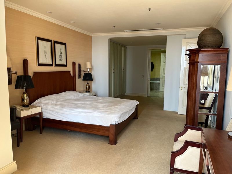 Spacious bedroom featuring built-in cupboards, textured wallpaper, and carpeted flooring, with an adjoining en-suite bathroom visible through the doorway.