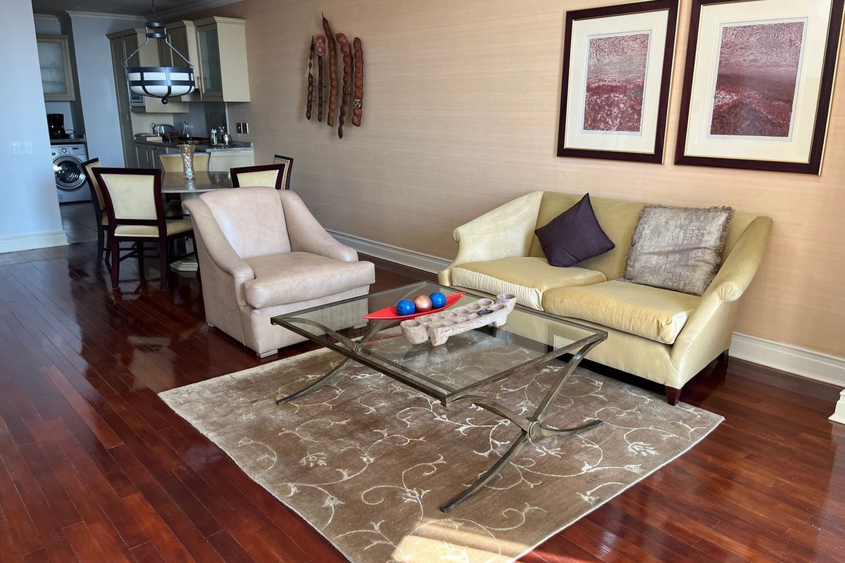 An open-plan living and dining area featuring polished hardwood flooring, crown molding, and a compact kitchen with built-in cabinetry and integrated laundry appliances.