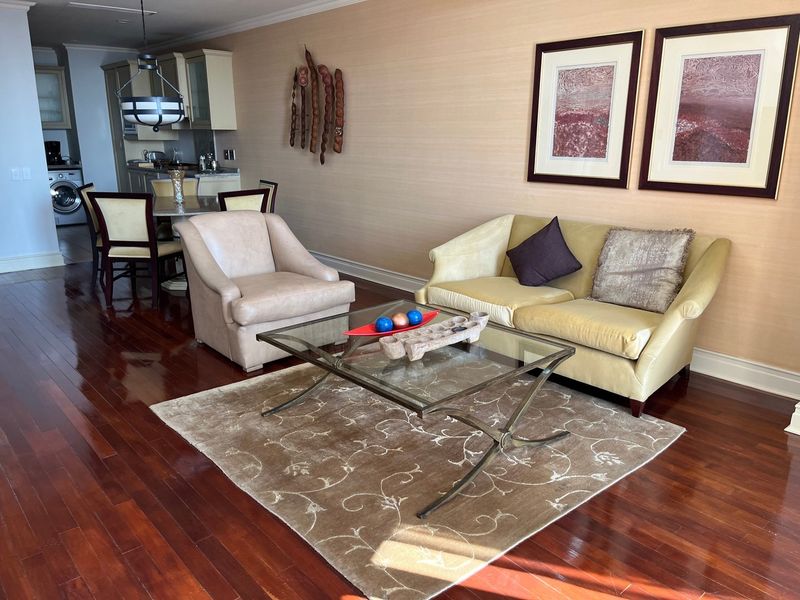 An open-plan living and dining area featuring polished hardwood flooring, crown molding, and a compact kitchen with built-in cabinetry and integrated laundry appliances.