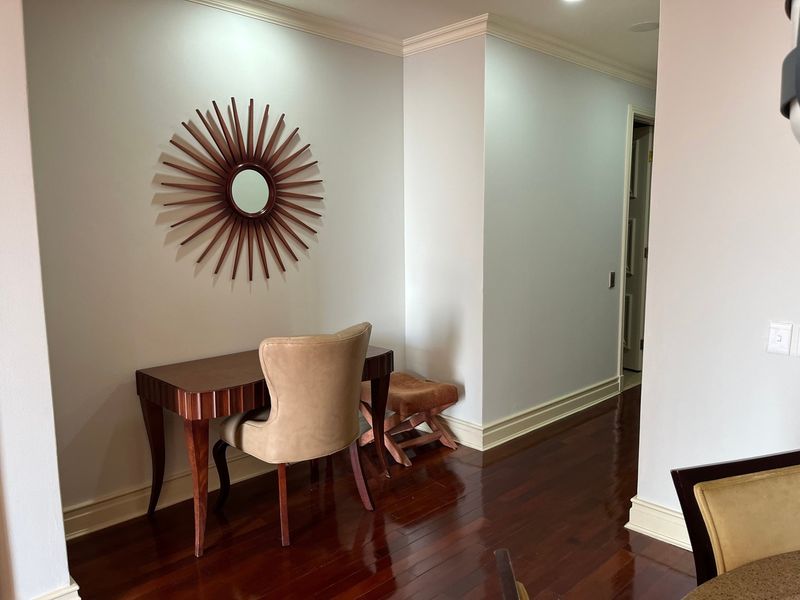 A well-maintained hallway featuring polished hardwood flooring, crown molding, and baseboards, creating a clean and transitionary space within the apartment.