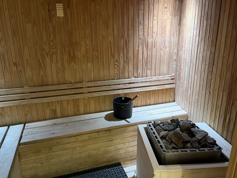A well-maintained private sauna featuring timber wall paneling, built-in wooden bench seating, and a dedicated sauna heater with stones.