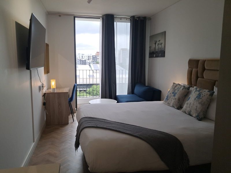 A well-maintained bedroom featuring elegant herringbone flooring, a large floor-to-ceiling window, and direct access to a private balcony.