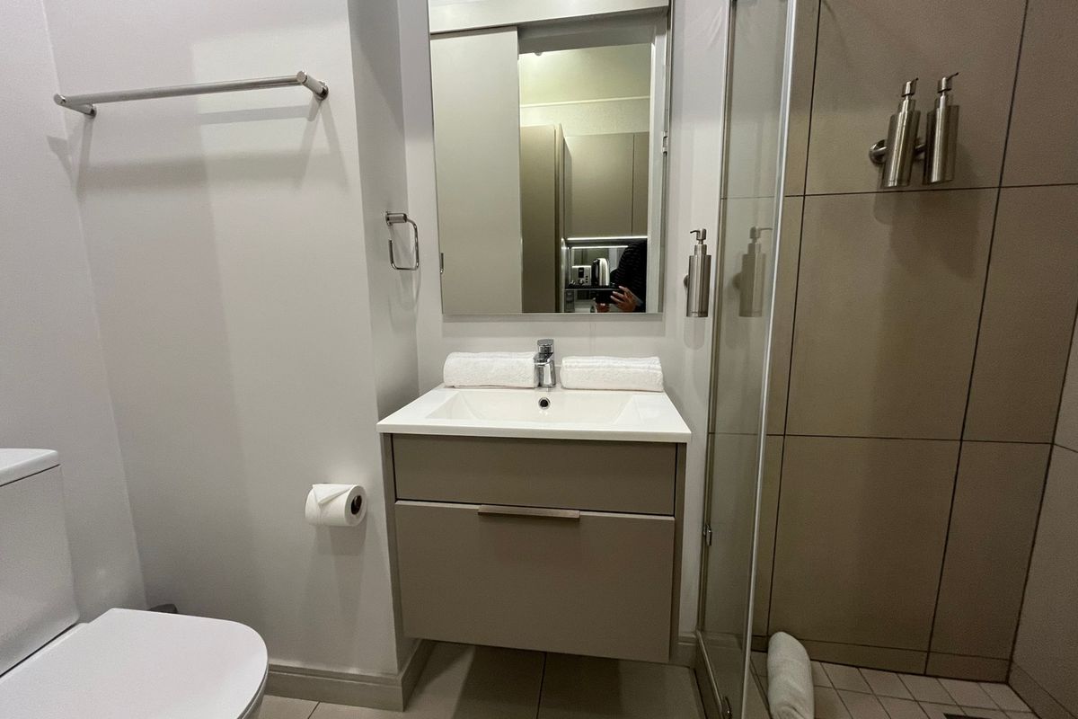 Modern bathroom featuring a wall-mounted vanity with integrated basin, frameless glass shower enclosure, and neutral floor-to-ceiling tiling.