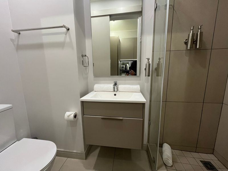 Modern bathroom featuring a wall-mounted vanity with integrated basin, frameless glass shower enclosure, and neutral floor-to-ceiling tiling.