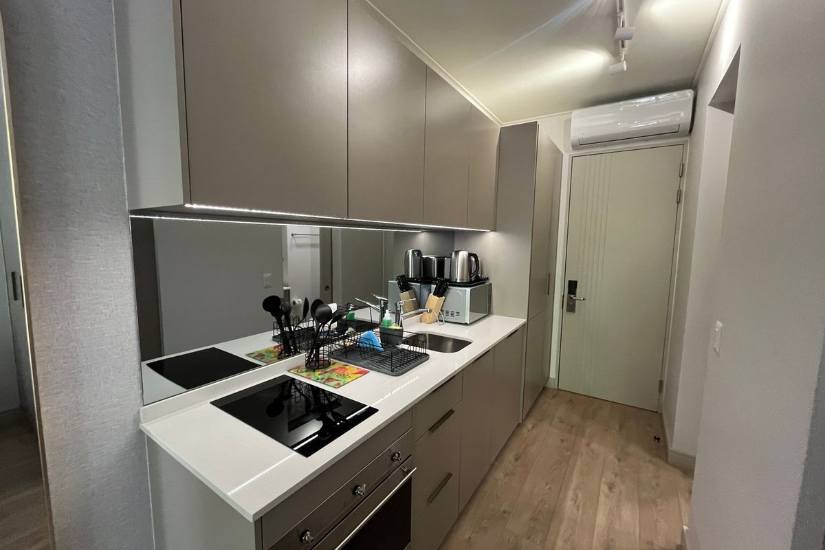 Modern compact kitchen featuring sleek handleless cabinetry, stone countertops, integrated induction hob, oven, and a stylish mirror splashback with under-cabinet lighting.