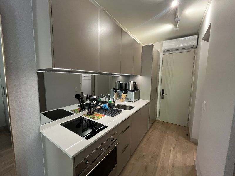 Modern compact kitchen featuring sleek handleless cabinetry, stone countertops, integrated induction hob, oven, and a stylish mirror splashback with under-cabinet lighting.