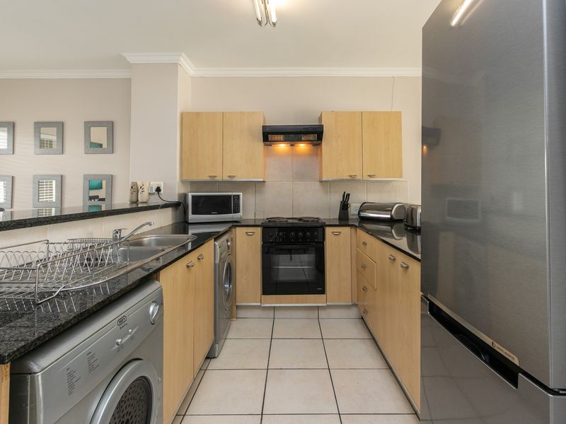 A functional kitchen featuring light wood cabinetry, granite countertops, tiled flooring, and integrated appliances, including a built-in oven and hob.