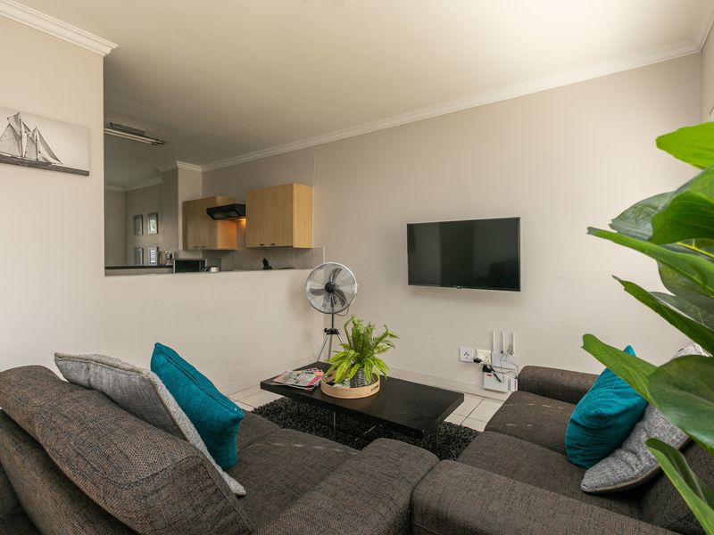 Open-plan living area featuring a pass-through window to the kitchen, neutral wall finishes, and tiled flooring throughout.