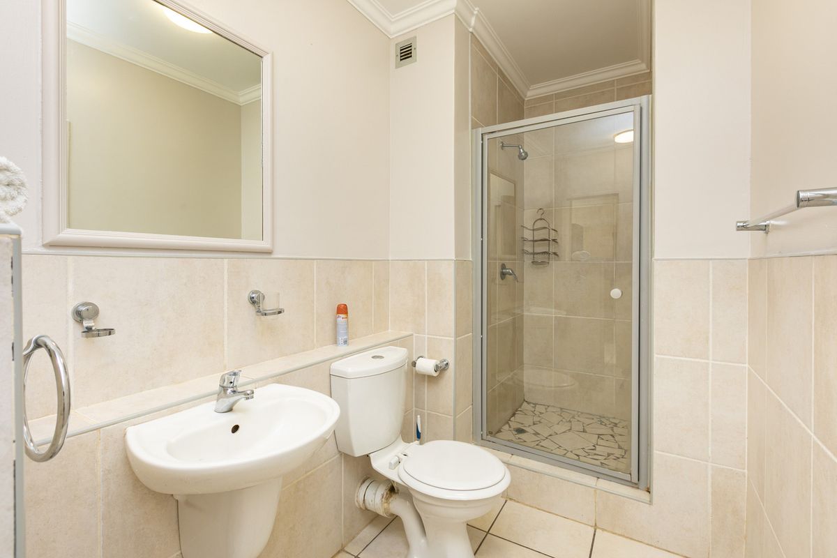 A functional bathroom featuring a pedestal basin, toilet, and a glass-enclosed shower with neutral wall and floor tiling.