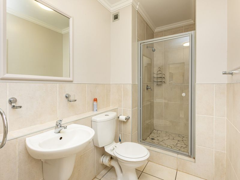 A functional bathroom featuring a pedestal basin, toilet, and a glass-enclosed shower with neutral wall and floor tiling.