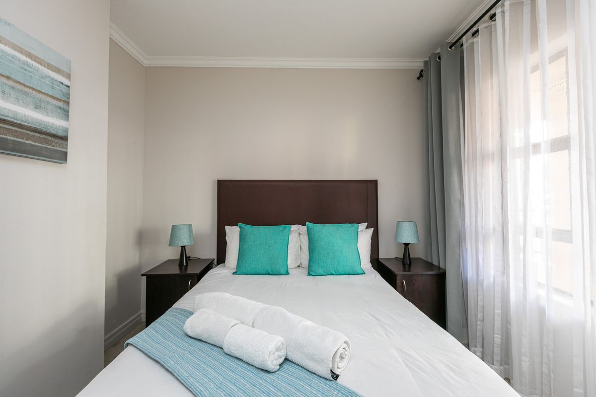 A well-maintained bedroom featuring neutral wall tones, crown molding, and large windows with layered curtains for natural light control.