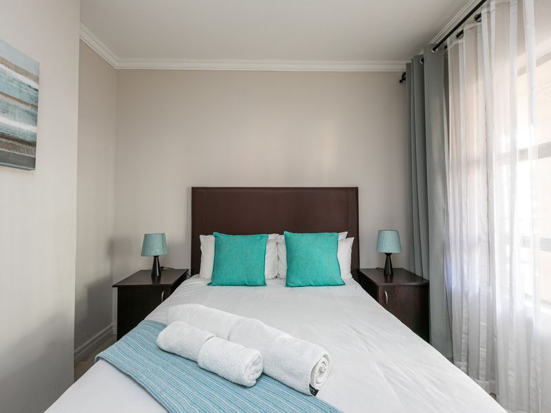 A well-maintained bedroom featuring neutral wall tones, crown molding, and large windows with layered curtains for natural light control.