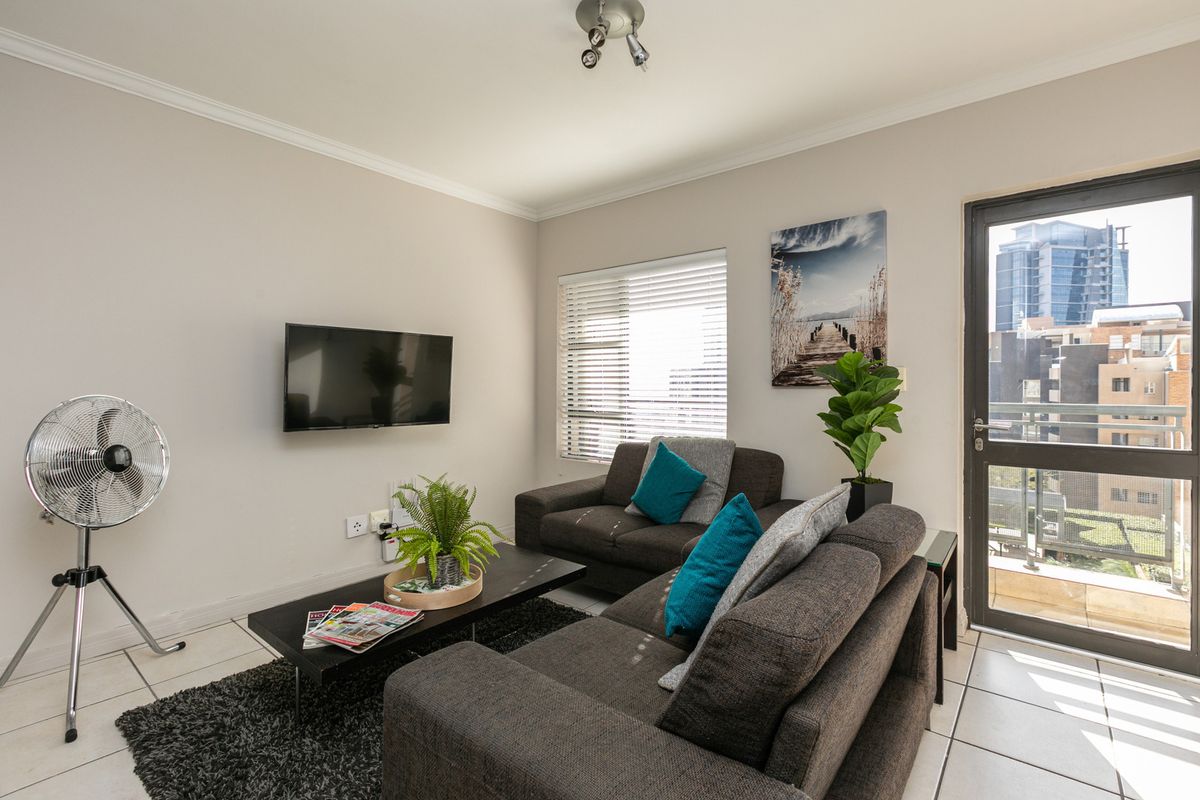 A well-maintained living room featuring tiled flooring, neutral walls, and direct access to an outdoor balcony through a glass panel door.