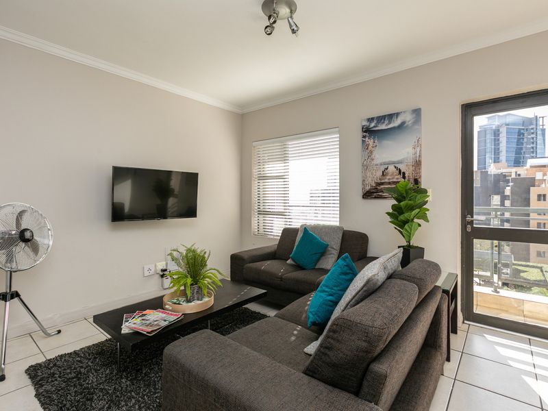 A well-maintained living room featuring tiled flooring, neutral walls, and direct access to an outdoor balcony through a glass panel door.