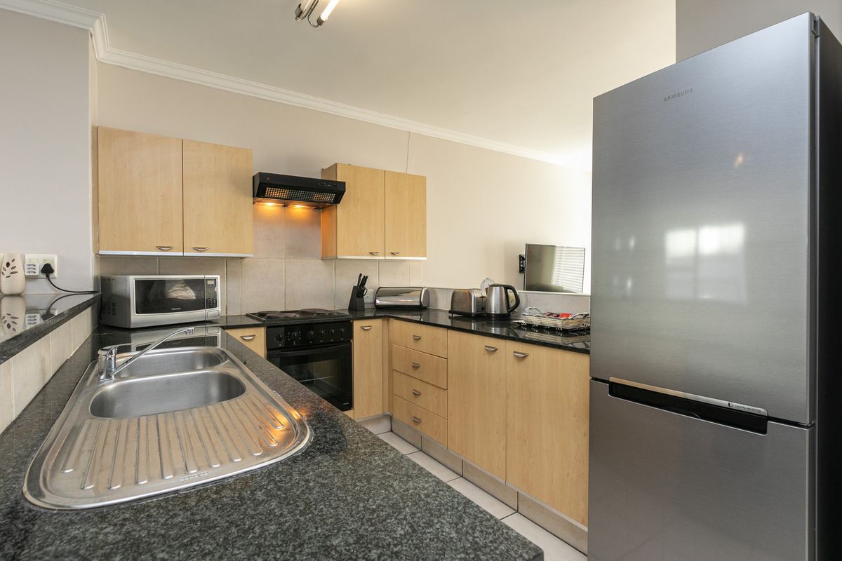 A functional kitchen featuring light wood cabinetry, dark granite countertops, a stainless steel double sink, and integrated cooking appliances.