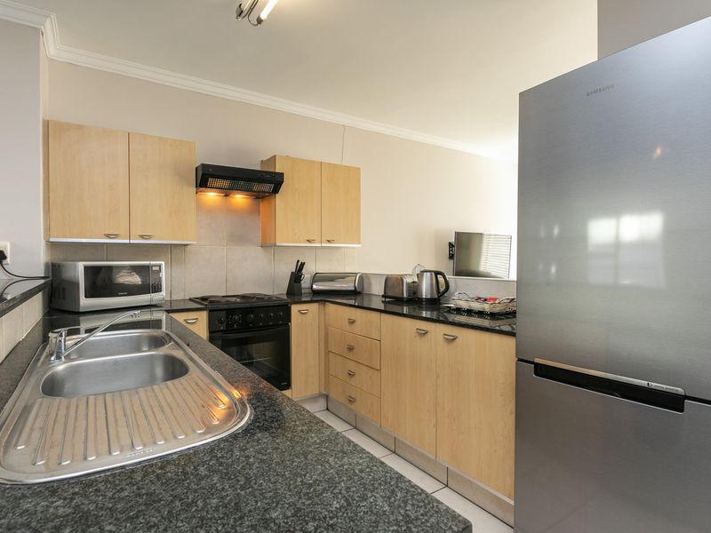 A functional kitchen featuring light wood cabinetry, dark granite countertops, a stainless steel double sink, and integrated cooking appliances.