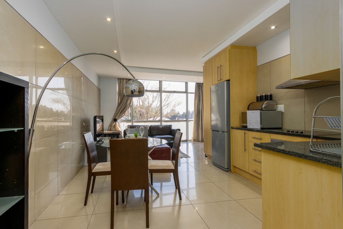Modern open-plan living area featuring a sleek kitchen with granite countertops, tiled flooring, and large glass doors leading to an outdoor space.