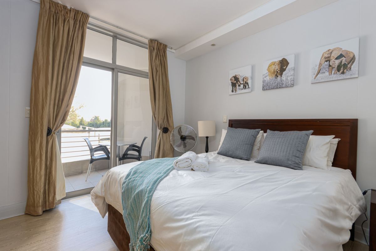 A well-lit bedroom featuring laminate flooring and a large sliding glass door providing direct access to a private balcony.