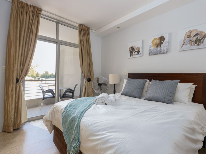 A well-lit bedroom featuring laminate flooring and a large sliding glass door providing direct access to a private balcony.