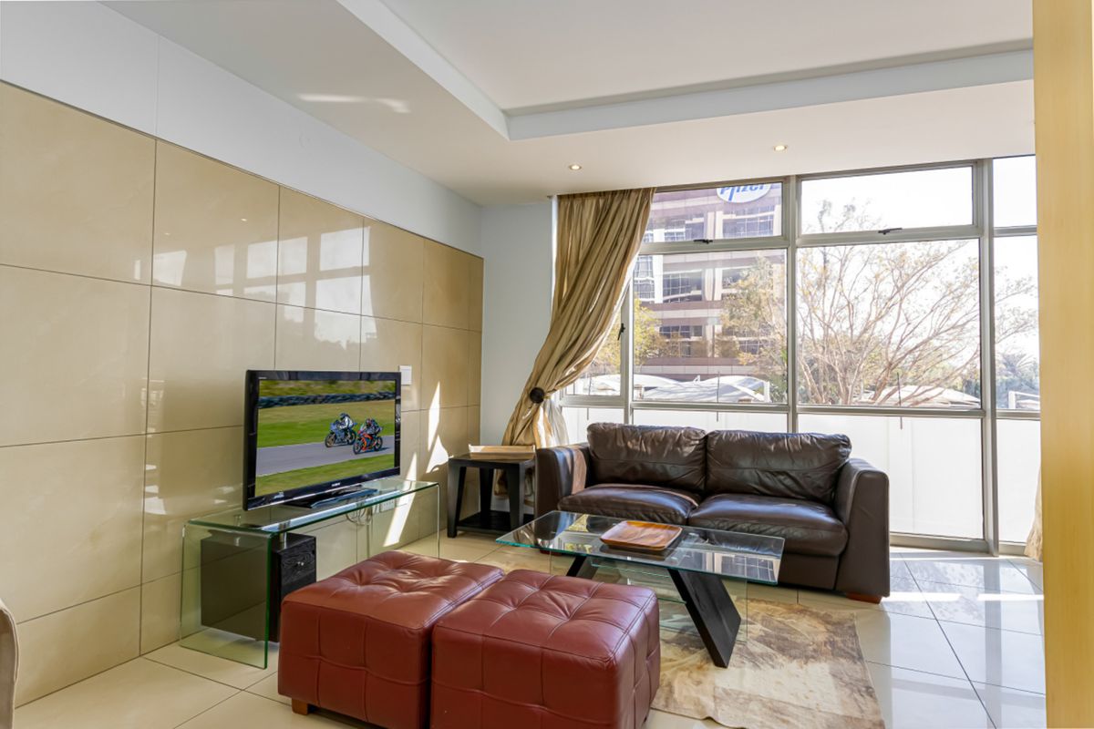 A bright living room featuring large windows, tiled flooring, and a modern feature wall, offering a comfortable and well-lit space.