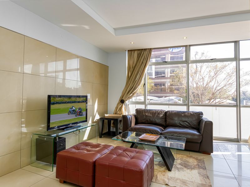 A bright living room featuring large windows, tiled flooring, and a modern feature wall, offering a comfortable and well-lit space.