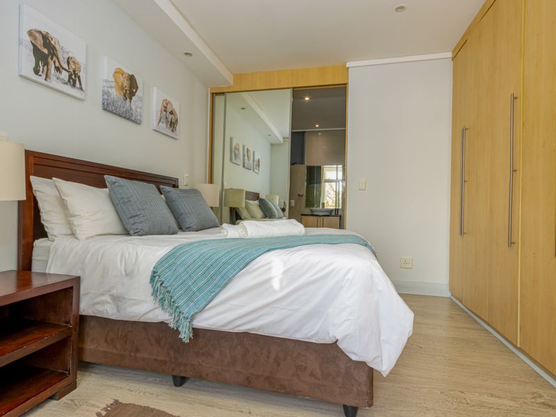 A well-maintained bedroom featuring light wood laminate flooring, extensive built-in cupboards with mirrored doors, and recessed ceiling lighting.