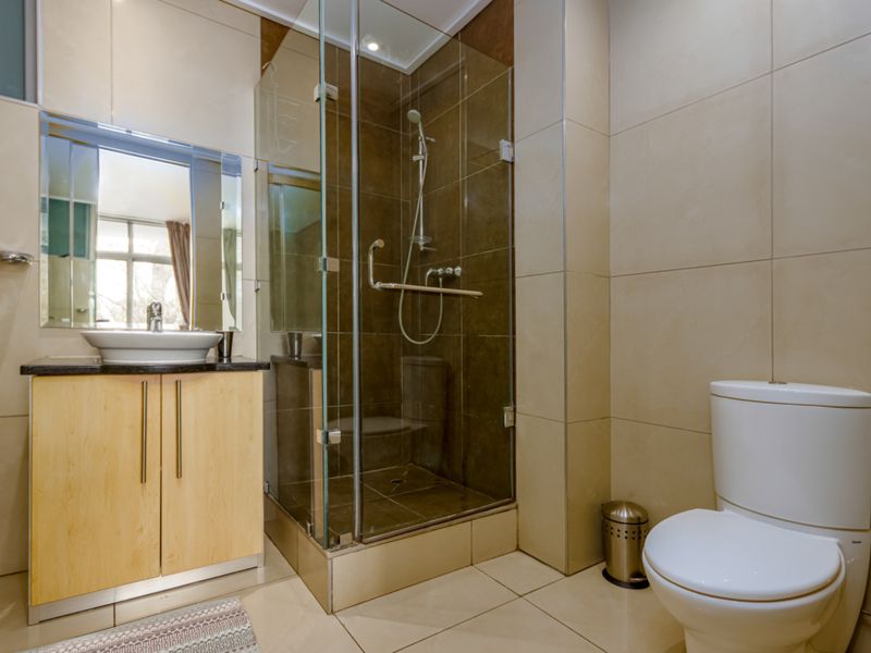 A modern bathroom featuring a glass-enclosed shower, a vanity cabinet with a countertop basin, and a standard toilet with neutral wall and floor tiling.